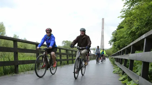 Group of people cycling alongside the river Boyne near Drogheda with the Boyne cable bridge in the background.