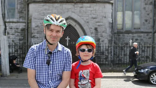 A man and a boy wearing cycling helmets in front of a church door